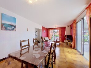 Ein Essbereich mit einem Glastisch, Stühlen, einer Couch und einem Fernseher.