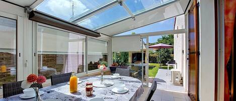 A covered patio with a table set for dining, large windows, and a view of the garden.