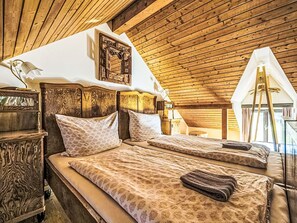 Une chambre avec un plafond en bois, un lit avec une literie à motifs, une table de chevet et une lampe fixée au mur.
