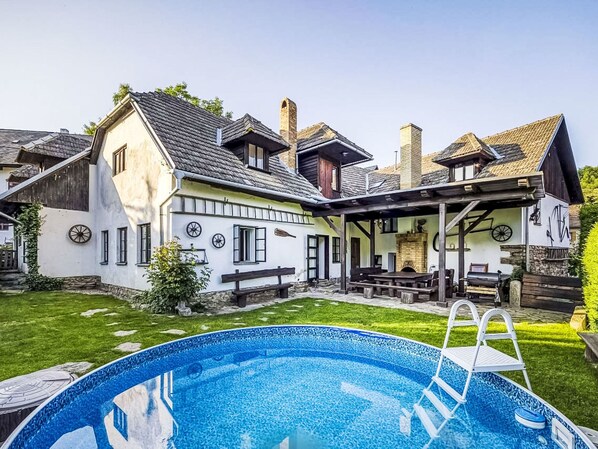Une maison avec une piscine, un patio couvert et une cheminée en pierre.