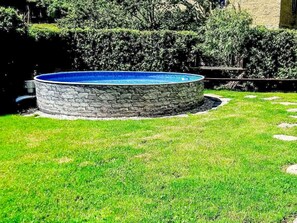 A circular stone pool with a blue interior, surrounded by a well-maintained lawn and stone edging.