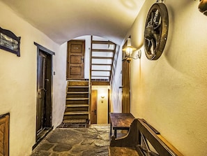 Un escalier en pierre mène à une chambre aménagée en mezzanine, dotée d’une lucarne, d’un banc en bois et d’un luminaire fixé au mur.