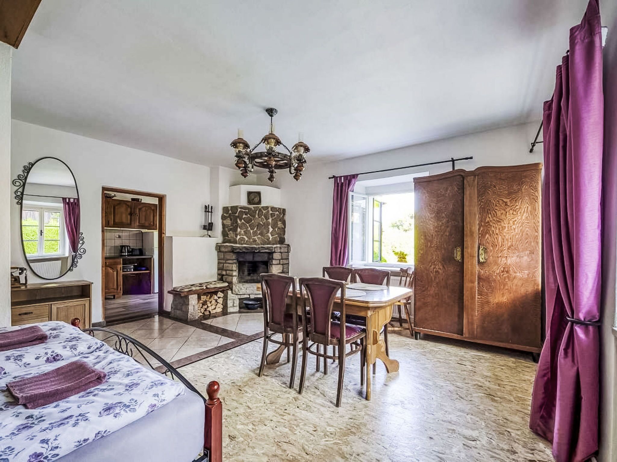 A bedroom with a bed, a dining table with chairs, a fireplace, and a wardrobe.