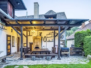 Un espace extérieur abrité, doté d’un sol en pierre, de bancs en bois et d’un barbecue.