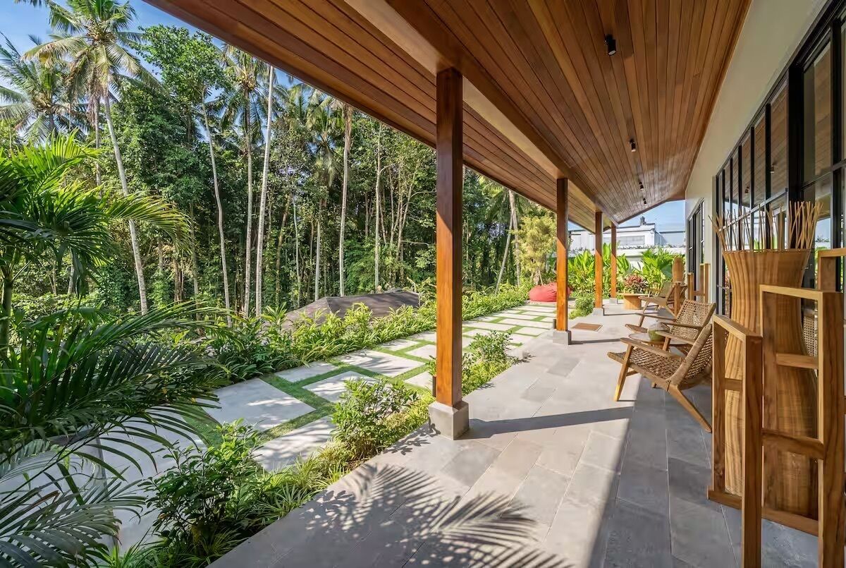 Un espacio al aire libre cubierto con pilares de madera, suelo de piedra y una zona de estar con mobiliario de mimbre.