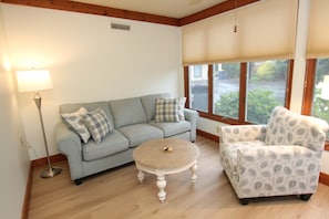Ein Wohnzimmer mit einer Couch, einem Sessel, einer Lampe und einem Fenster mit Jalousien.