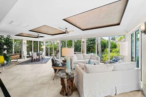 A spacious living area with a large window, a ceiling fan, and a dining area with a table and chairs. - Las Olas Waterfront Home | Heated Pool, Yacht Dock (Fort Lauderdale)