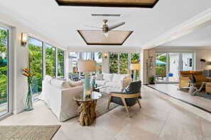 A spacious living area with a ceiling fan, large windows, and a view of greenery. - Las Olas Waterfront Home | Heated Pool, Yacht Dock (Fort Lauderdale)
