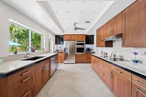 A modern kitchen with wooden cabinets, stainless steel appliances, and a large window providing natural light. - Las Olas Waterfront Home | Heated Pool, Yacht Dock (Fort Lauderdale)