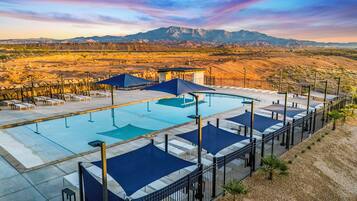Zona de piscina con sillas de descanso y sombrillas, rodeada por una valla, con montañas al fondo.