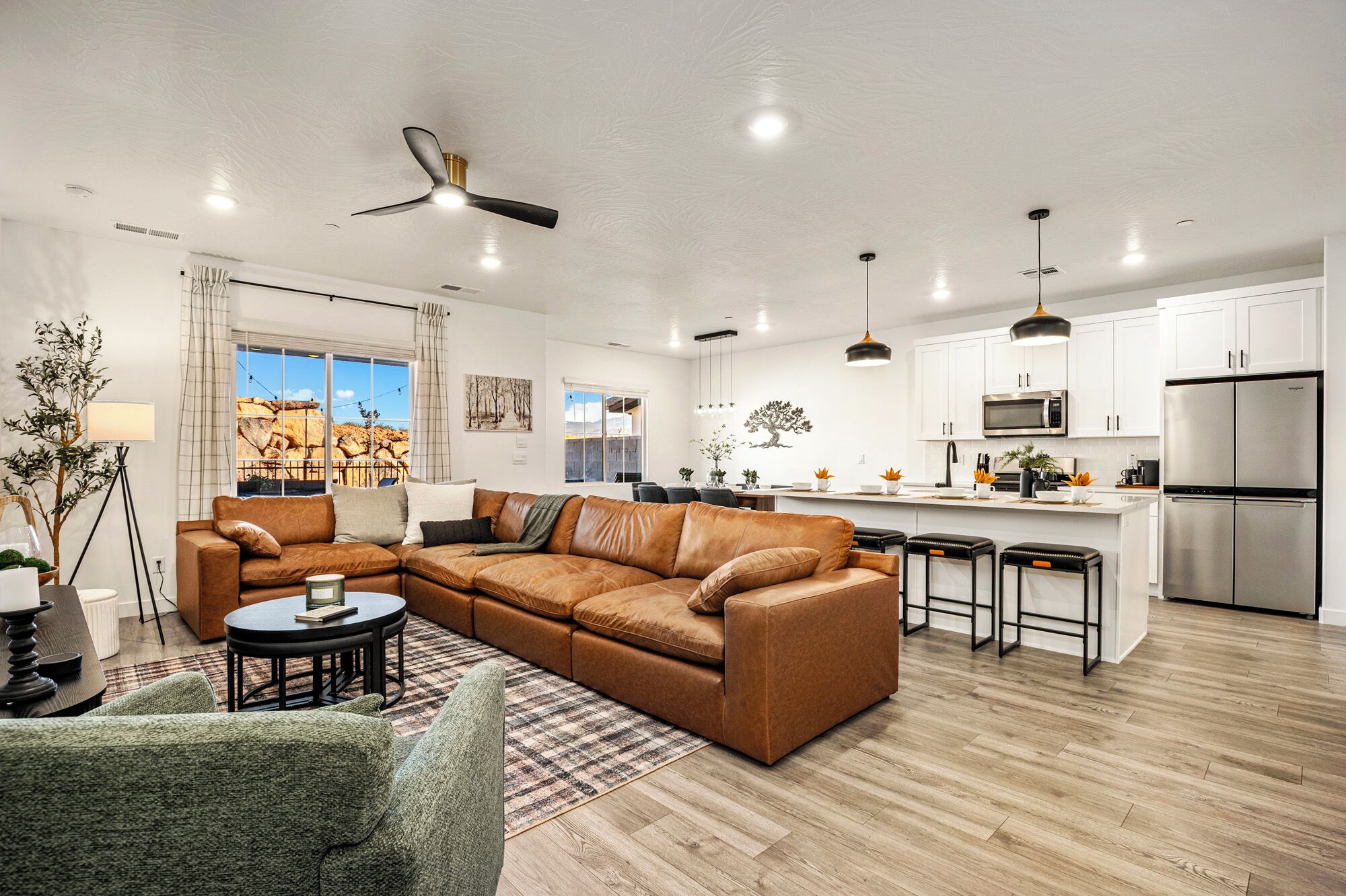 A modern living room with a sectional sofa, a dining area, and a kitchen with stainless steel appliances.