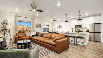 A modern living room with a sectional sofa, a dining area, and a kitchen with stainless steel appliances.