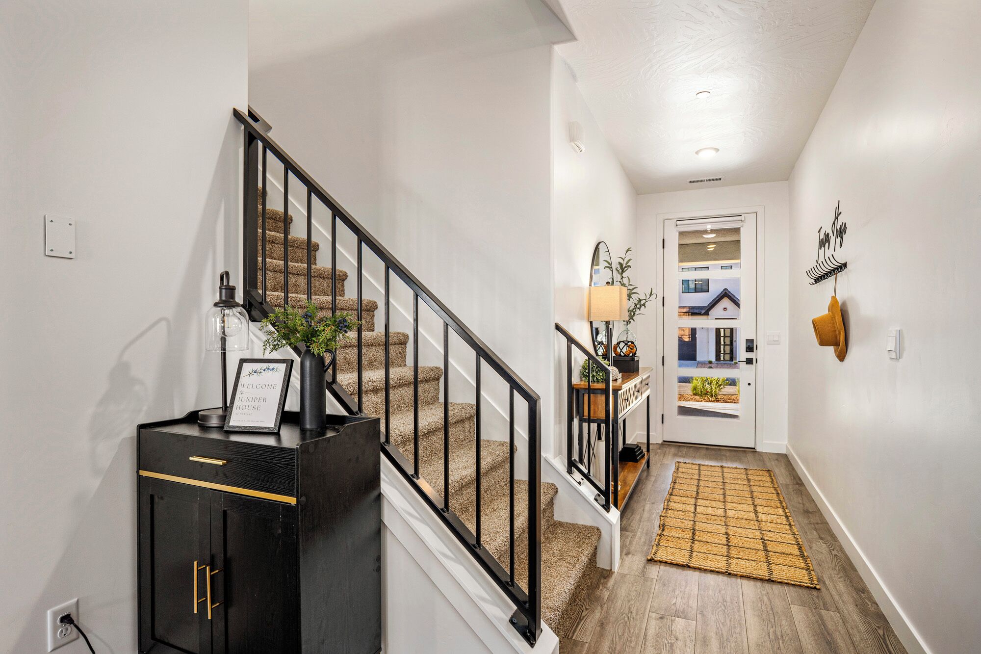 A hallway with a staircase, a welcome sign, a lamp, and a rug.