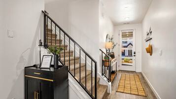 A hallway with a staircase, a welcome sign, a lamp, and a rug.