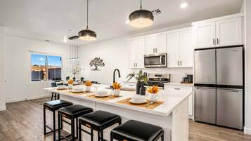 A modern kitchen with white cabinets, a stainless steel refrigerator, and a central island with bar stools.