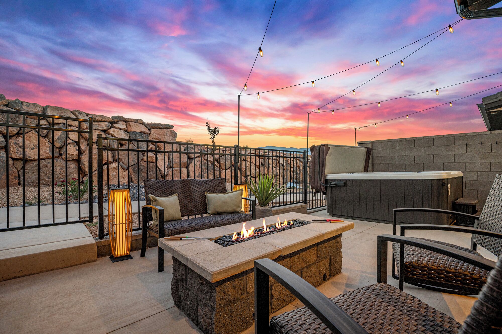 A patio with a fire pit, outdoor seating, string lights, and a view of the desert landscape.