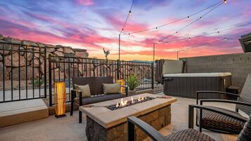 A patio with a fire pit, outdoor seating, string lights, and a view of the desert landscape.