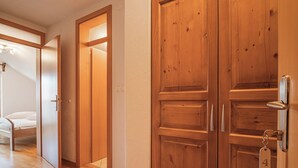 Eine Holztür mit Schlüsselloch und Klingel, ein hölzernes Bett und ein Korridor mit Holzboden.