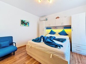 A bedroom with a bed, a blue sofa, a painting, an air conditioning unit, and a wardrobe. - Apartment Palma by Interhome (Stanići)