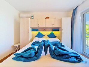 Hotellihuone, jossa on sänky, pieni pöytä, ikkuna verhoilla ja kattoon asennettu ilmastointilaite.