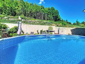 A clear blue pool with a stone wall and a wooden deck with chairs and a table. - Apartment Palma by Interhome (Stanići)