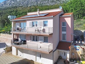 A multi-story building with balconies, a stone wall, and a mountainous backdrop. - Apartment Palma by Interhome (Stanići)