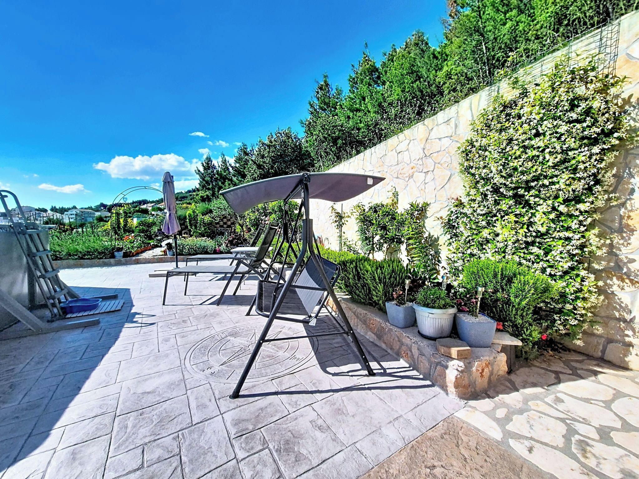 An outdoor patio with a stone floor, a metal chair, a table, and a wall covered in greenery.