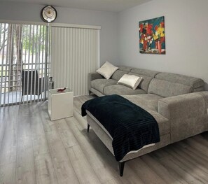 Ein modernes Wohnzimmer mit grauem Sofa, einem weißen Beistelltisch, einer schwarzen Decke, einem Bild an der Wand und einem Fenster mit Jalousien.