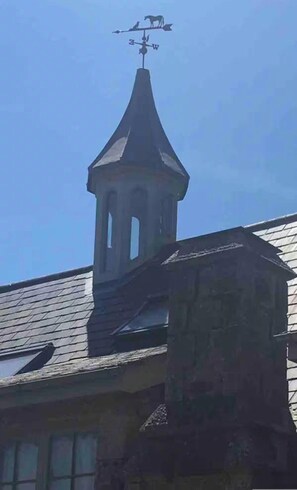 A building with a weather vane on top and a tower with arched windows.