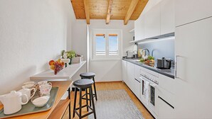 A kitchen with white cabinets, a wooden ceiling, a window, and a countertop with a pot and a kettle. - Agra Apartment (Lugano), Agra -Lugano, Switzerland (Agra -Lugano)