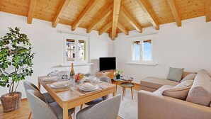 A dining area with a wooden table set for four, a sofa, and a television in a room with wooden beams on the ceiling. - Agra Apartment (Lugano), Agra -Lugano, Switzerland (Agra -Lugano)