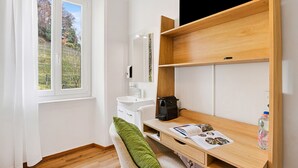 Una stanza con finestra, lavandino bianco, specchio, scrivania in legno e un cuscino verde.