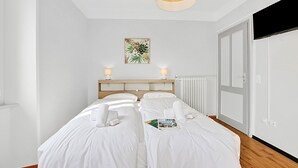 A hotel room with two beds, a wooden headboard, a radiator, a door, and a wall-mounted artwork. - Agra 7 (Lugano), double, Private Bathroom, Agra -Lugano, Switzerland (Agra -Lugano)