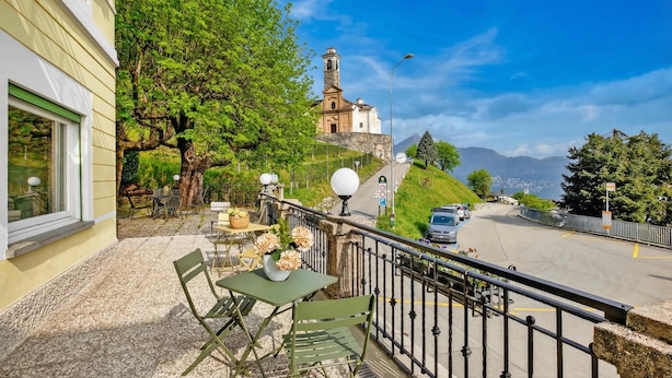 A balcony with outdoor seating, a view of a church, and a road with cars. - Agra 6 (Lugano), single, Shared Bathroom, Agra -Lugano, Switzerland (Agra -Lugano)