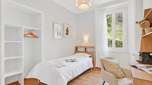 A bedroom with a bed, a chair, a desk, a wardrobe, and a window with a view. - Agra 5 (Lugano), single, Shared Bathroom, Agra -Lugano, Switzerland (Agra -Lugano)