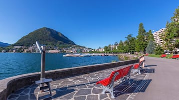 A waterfront promenade with stone flooring, red benches, and a view of a mountain and cityscape across the water.