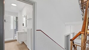Een trap die leidt naar een badkamer met een douche, toilet en wastafel.
