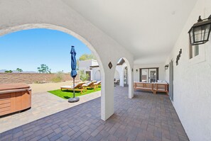 Eine überdachte Terrasse mit Whirlpool, Liegestühlen und einer hölzernen Bank.