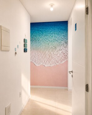 Ein Flur mit einem Wandgemälde vom Strand, einer Tür rechts und einer Deckenleuchte.