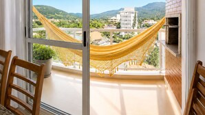 En balkon med en gul hængekøje, en potteplante og udsigt til bygninger og bjerge.