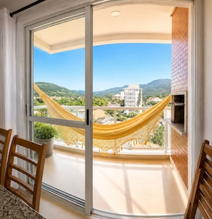 Ein Balkon mit einer gelben Hängematte, einem Topfpflanzen und Blick auf Gebäude und Berge.