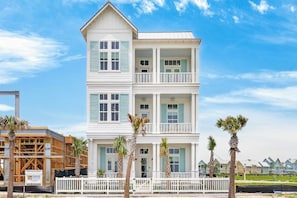 A multi-story building with a balcony on the second floor, surrounded by palm trees. - Multilevel beach house with water view, balconies, WIFI, kitchen and shared pool (Port Aransas)