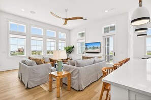 A spacious living room with a large sofa set, a wooden coffee table, a TV, and a kitchen area with a white island and bar stools. - Multilevel beach house with water view, balconies, WIFI, kitchen and shared pool (Port Aransas)