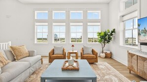 Un salón amplio con un gran ventanal, un sofá, dos sillones, una mesa de centro y un televisor.
