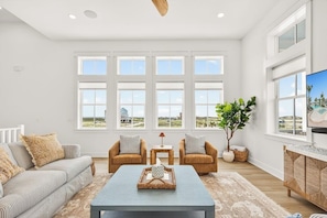 A spacious living room with a large window, a sofa, two armchairs, a coffee table, and a TV. - Multilevel beach house with water view, balconies, WIFI, kitchen and shared pool (Port Aransas)
