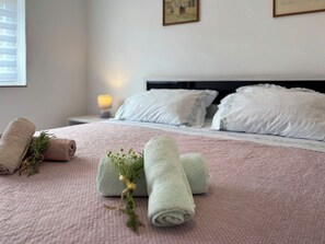 A neatly made bed with rolled towels and a small plant, a bedside lamp, and a framed picture on the wall. - Jadranka by Interhome (Opatija/Pobri)