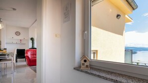 Ein modernes Wohnzimmer mit Essbereich, einem roten Sessel, einer kleinen Holzhaus-Dekoration und Blick auf das Meer durch ein großes Fenster.
