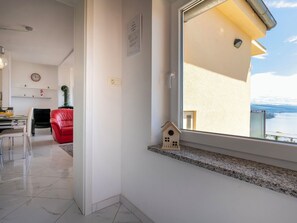 A modern living room with a dining area, a red chair, a small wooden house decoration, and a view of the sea through a large window. - Jadranka by Interhome (Opatija/Pobri)