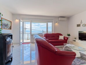 Ein modernes Wohnzimmer mit einem roten Sofa, einem Glastisch, einem Fernseher und einem Balkon mit Blick.