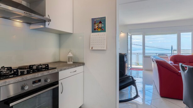 Eine moderne Küche mit Gasherd, Backofen und weißen Schränken. An der Wand hängt ein Kalender und es gibt einen Blick auf den Balkon mit roter Möbel.